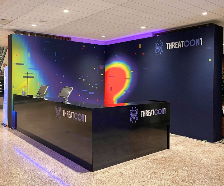 Custom-designed THREATCON1 registration desk with colorful branded backdrop at Sheraton Reston, Virginia. Spatial design and event production by Layout21